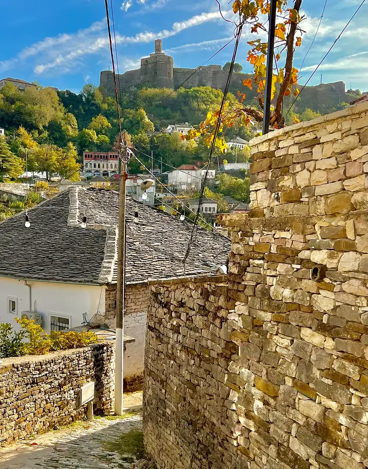 A steep cobbled lane between stone walls in Gjirokastër with the castle on the ridge above