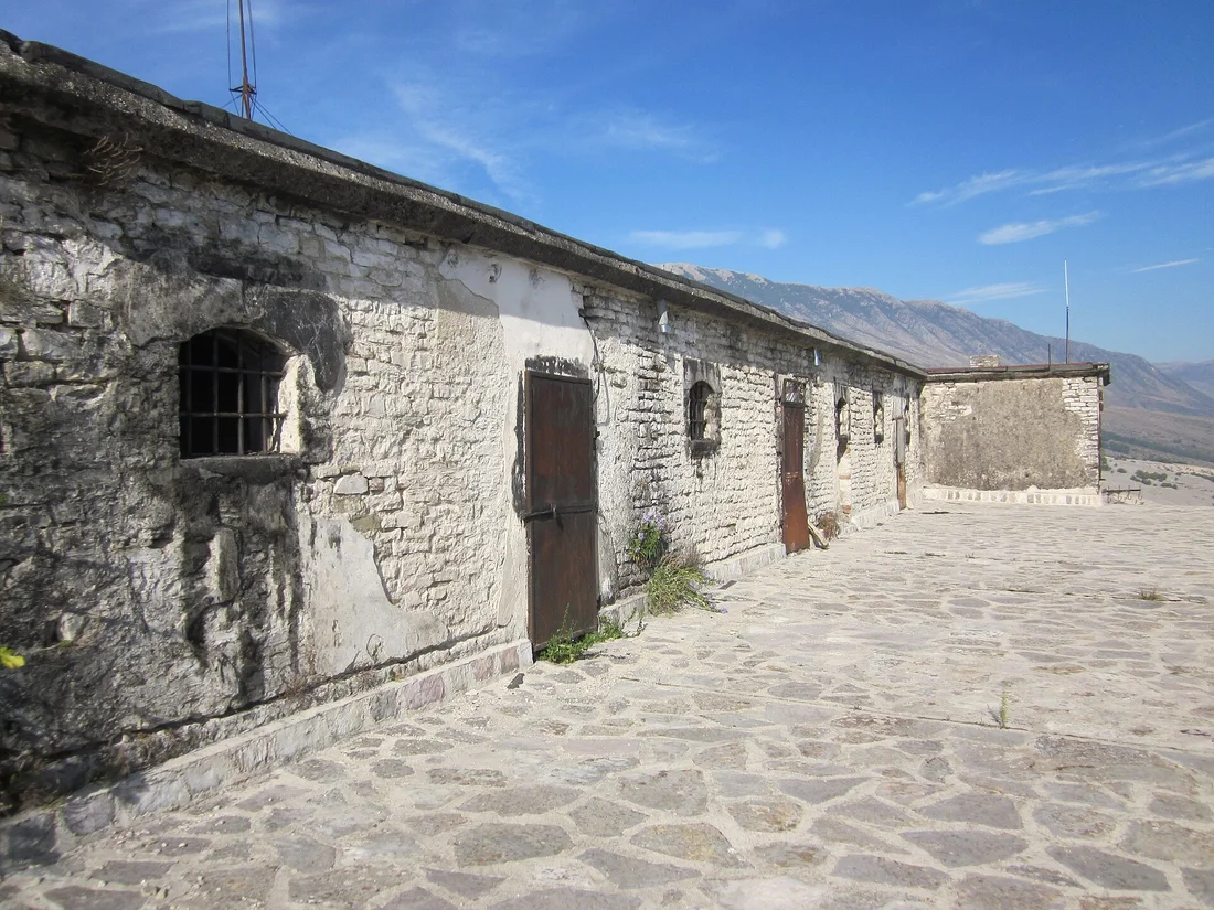 Long low stone prison building with barred windows on a sunny courtyard