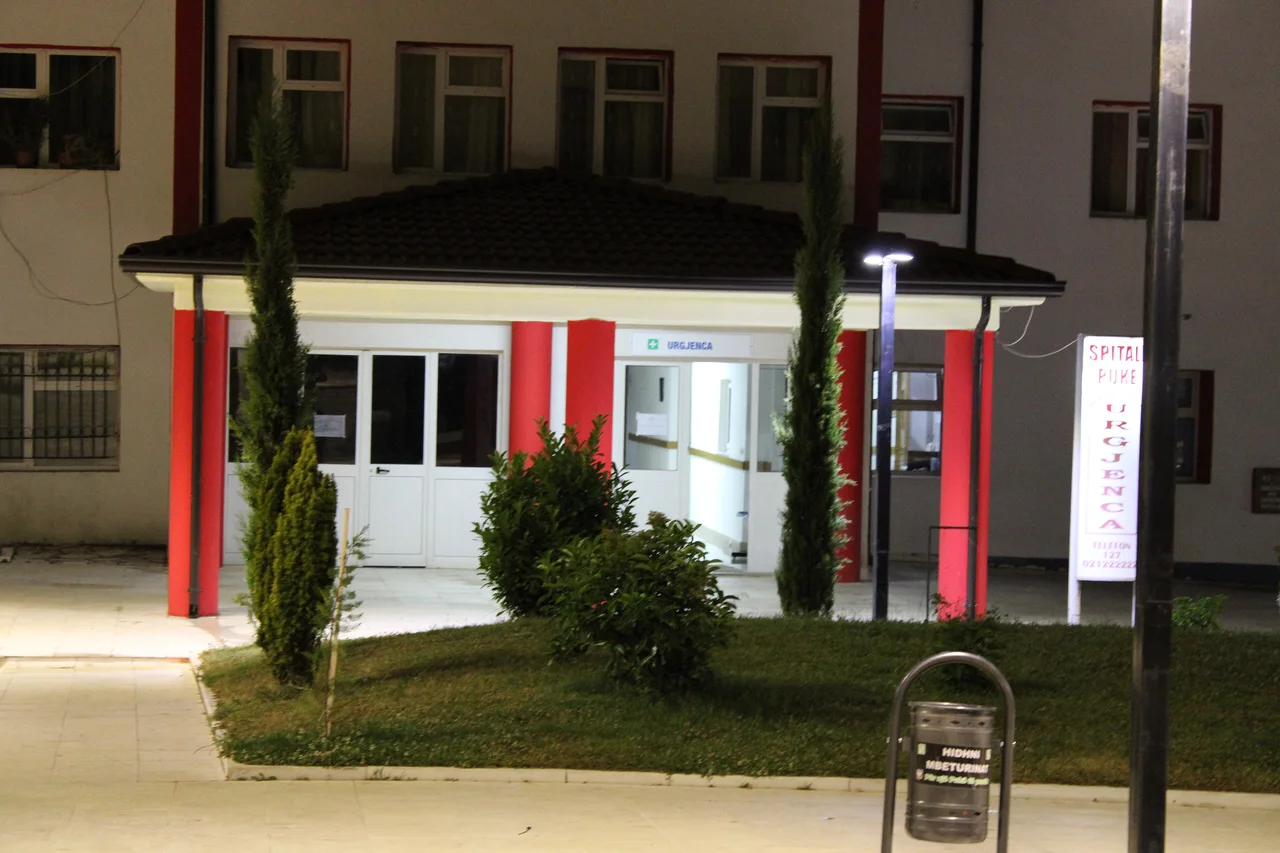 Illuminated emergency entrance of the public hospital in Puke, northern Albania, with an URGJENCA sign and a 127 phone number on the noticeboard