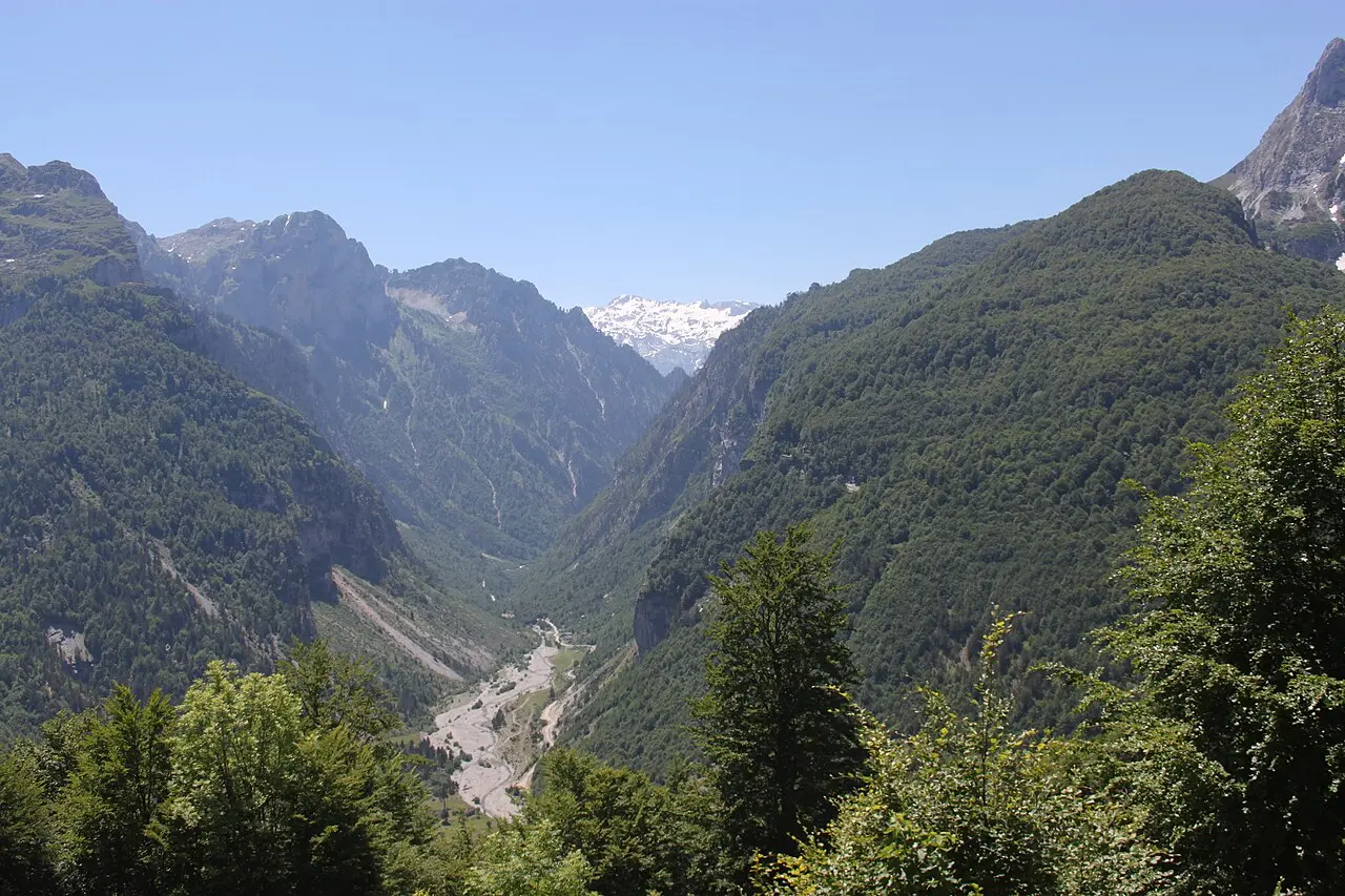 The green Çerem valley in the Albanian Alps with forested slopes and a dirt track