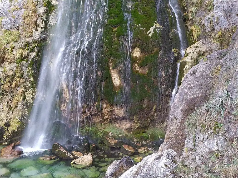 Grunas waterfall dropping over a rock lip into a pool in the woods near Theth