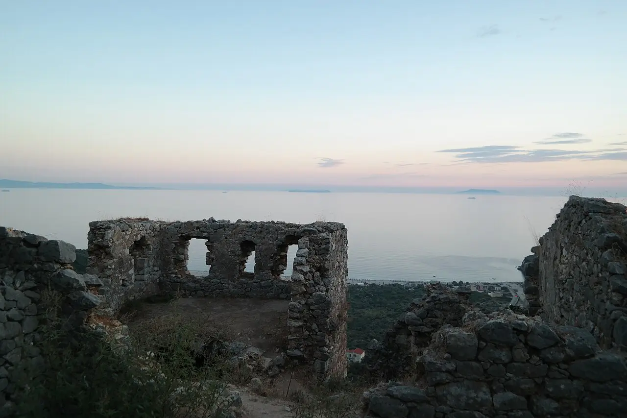 The ruined walls of Himara castle at dusk, the Ionian Sea glowing pink beyond and the town below
