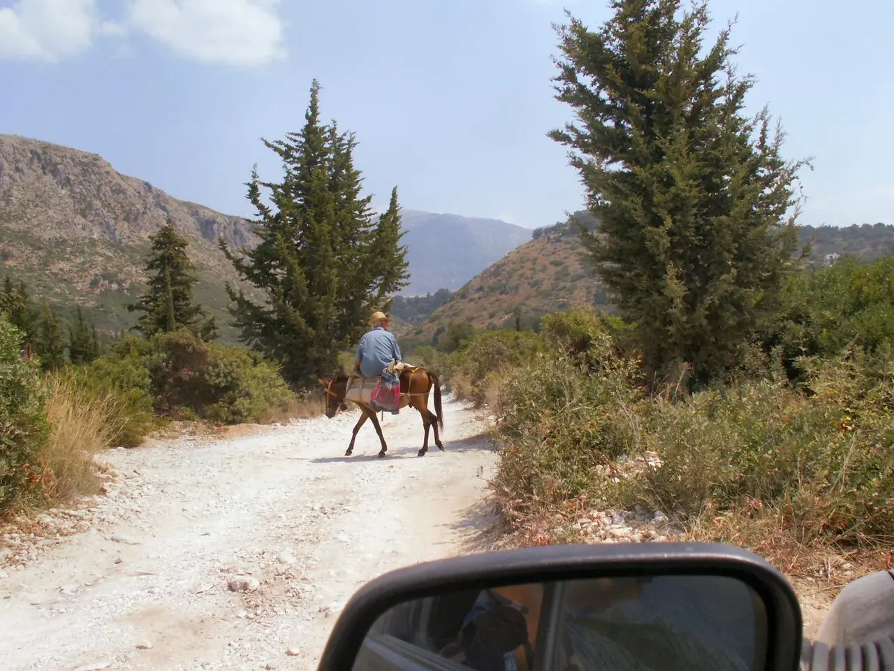 A man on a mule crossing a dusty backcountry track in the hills above Himara