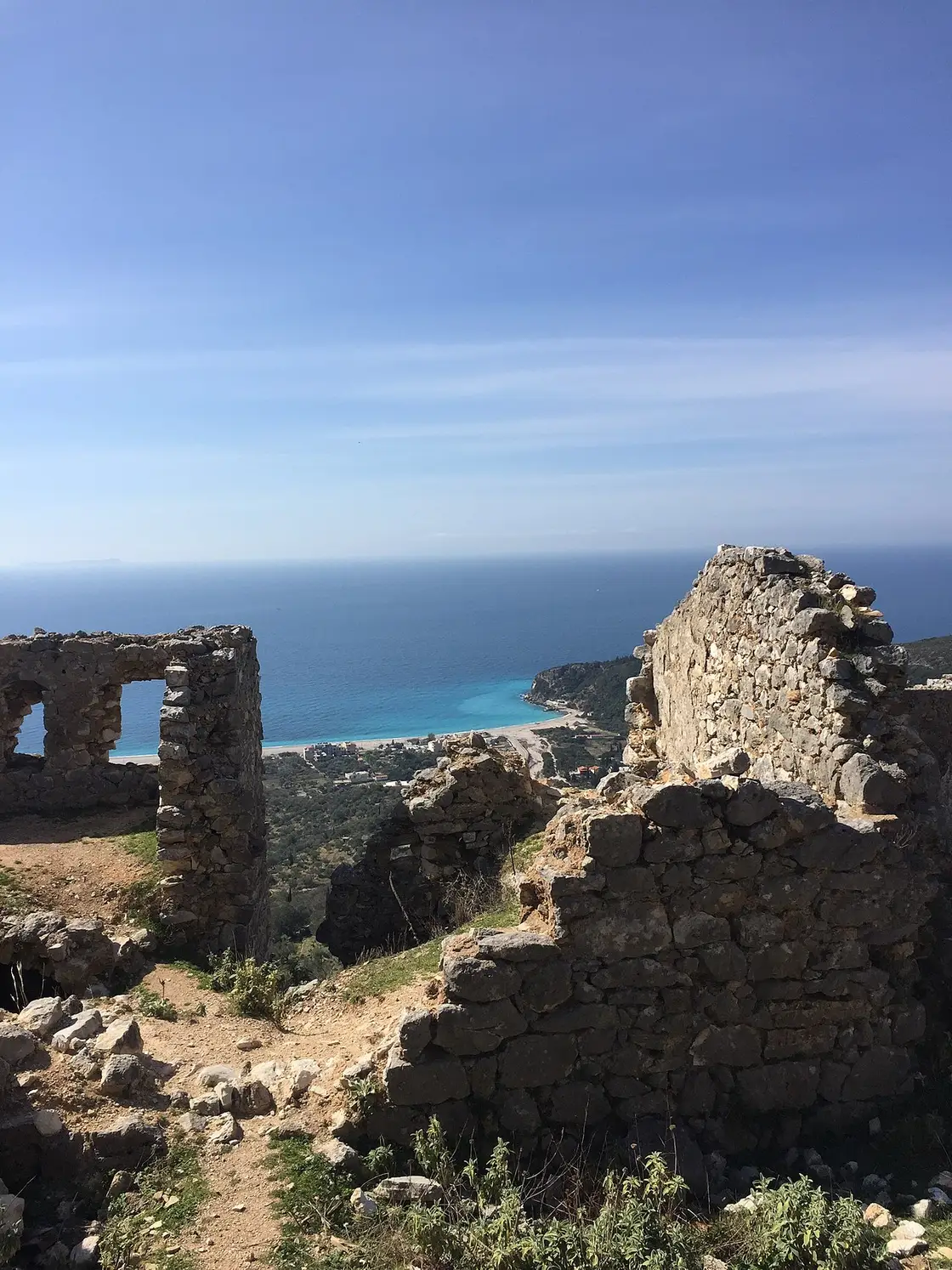 Stone ruins of Himara castle on the hilltop with a turquoise beach and coast far below