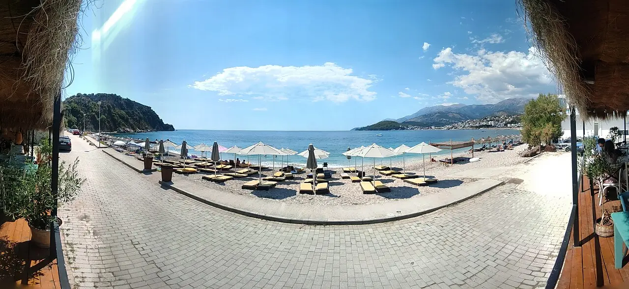 Sunbeds and umbrellas on the pebble beach at Potami near Himara, with a turquoise bay and headland