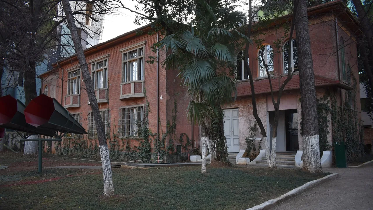 The red-brick House of Leaves museum in Tirana behind its garden, with two red horn-shaped sculptures on the lawn