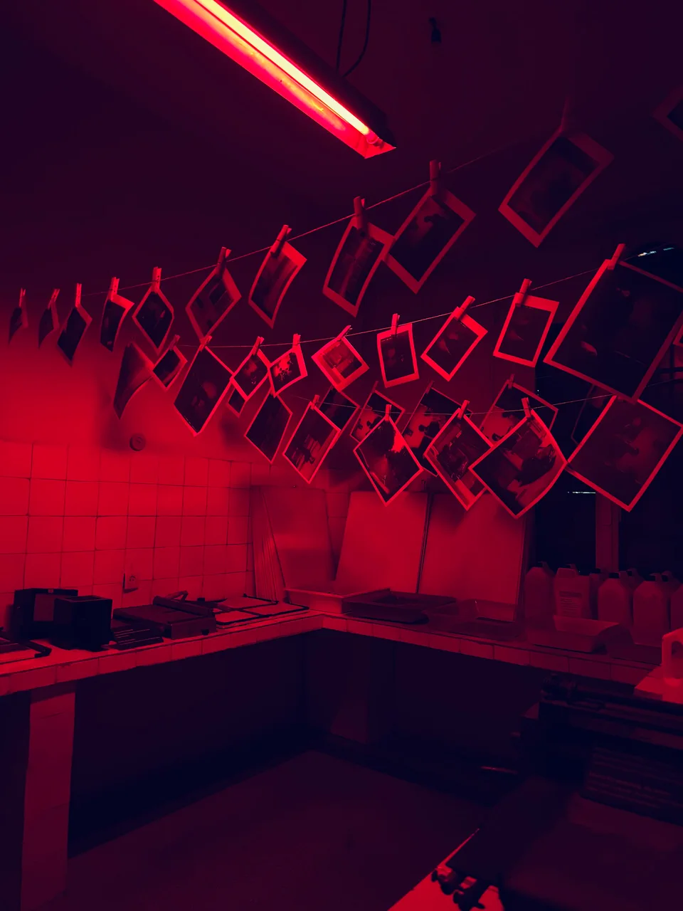 A darkroom lit red with photographic prints hanging from lines above a tiled workbench