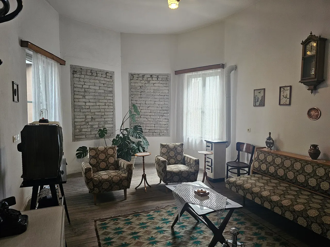 A 1970s Albanian living room with patterned armchairs, a sofa, a rug and a wall clock