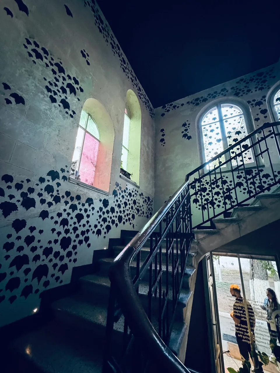 The stairwell of the House of Leaves with dark leaf shapes stencilled across pale walls and arched windows
