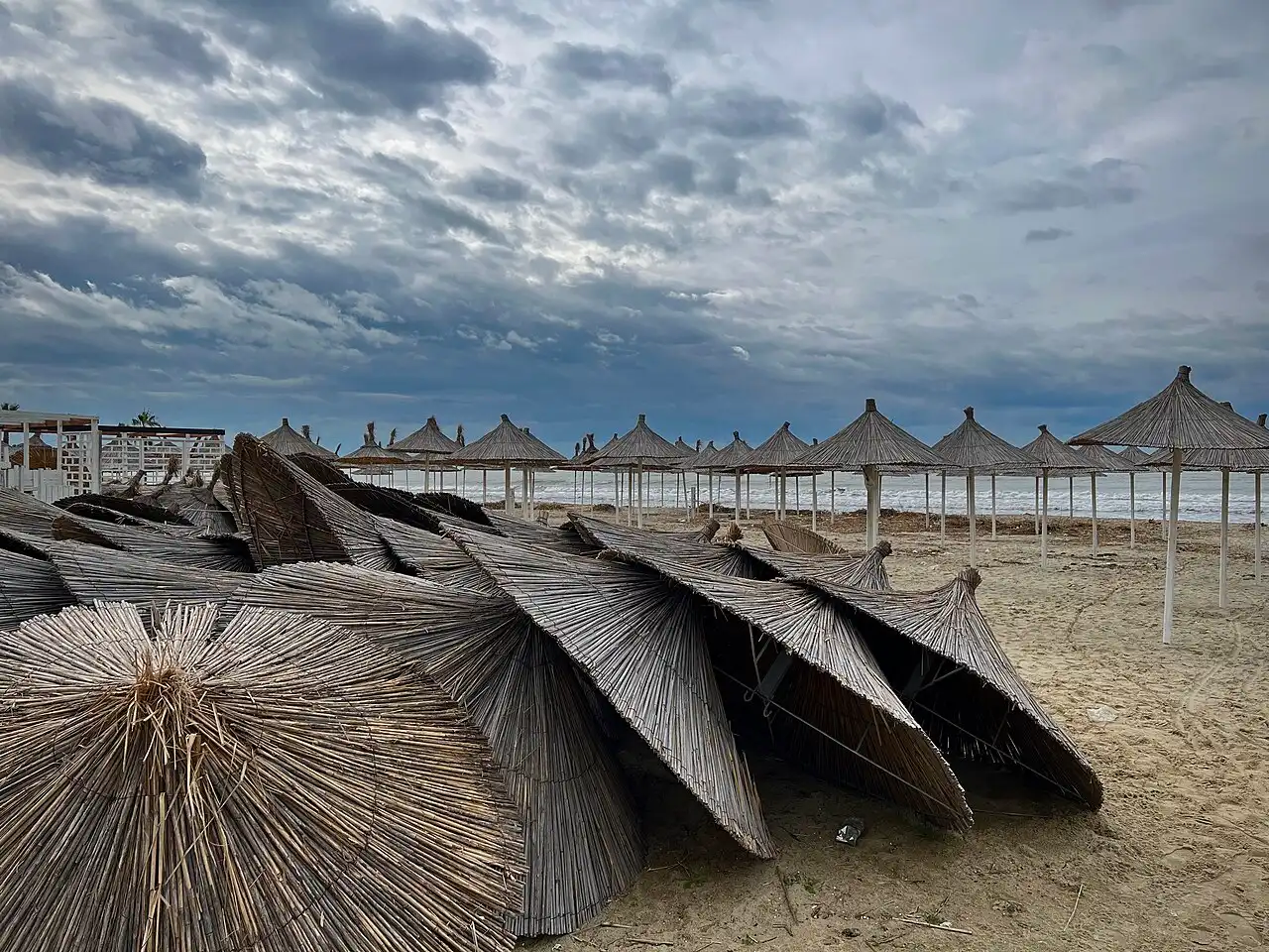 Stacked beach umbrellas at Golem on Albania's coast with sand, beach equipment and the Adriatic Sea nearby