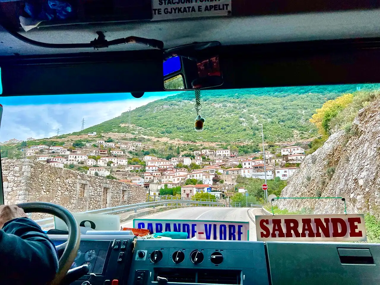 A mountain road above Vuno on the Albanian Riviera with green hills and the Ionian coast in the distance