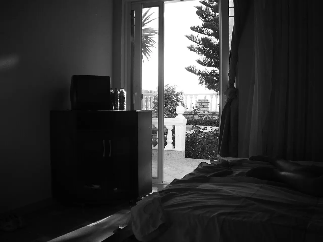 A simple hotel room in Saranda with a double bed, tiled floor and balcony light coming through the window