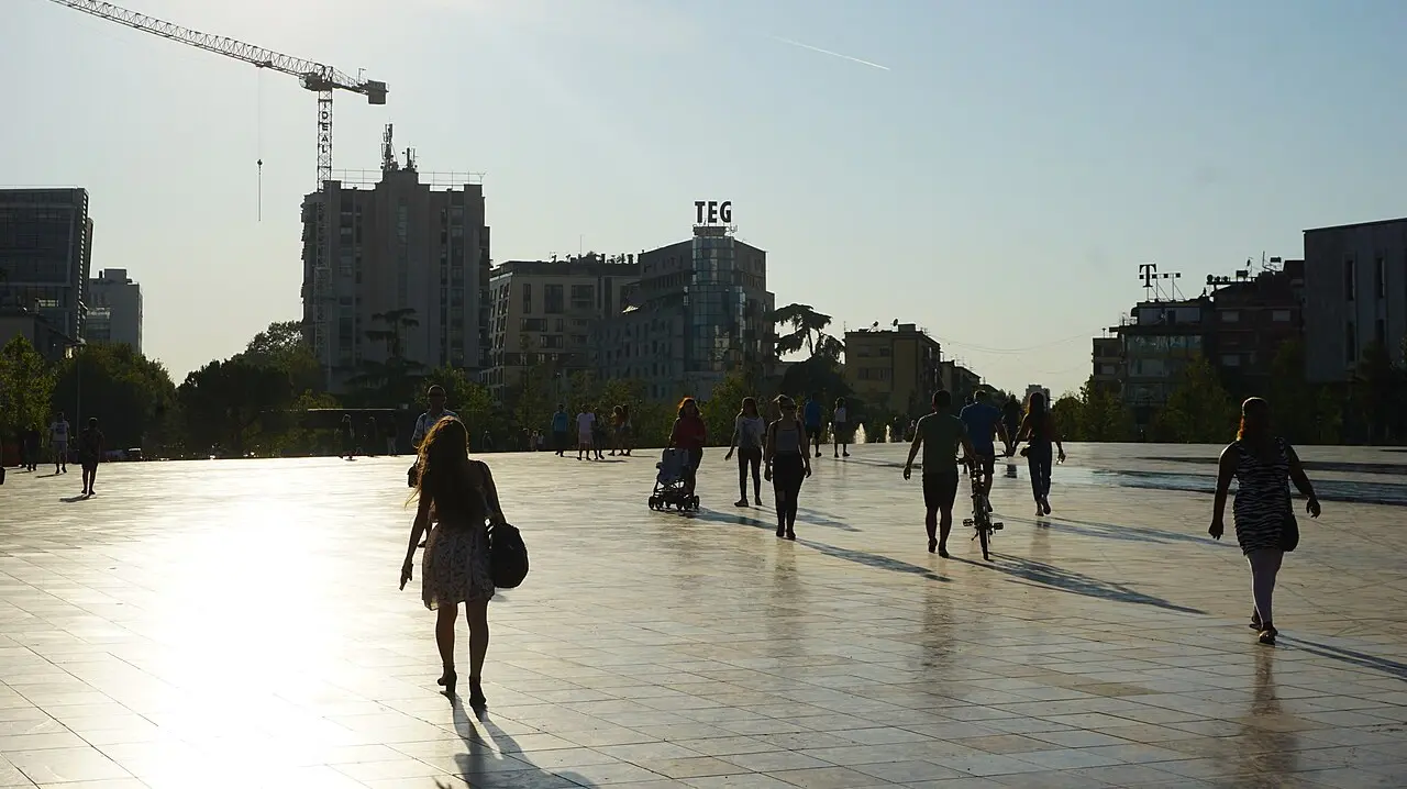 People strolling across the wide pedestrian expanse of Skanderbeg Square in central Tirana on a sunny evening
