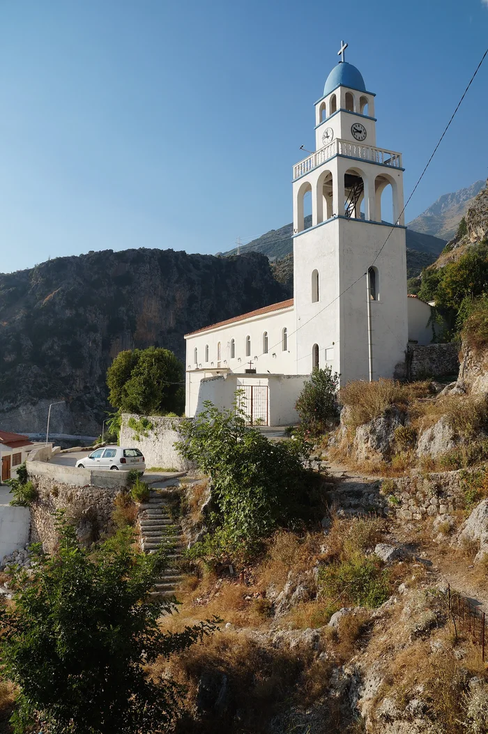 White bell tower of the church of Saint Spyridon above Dhërmi against a blue sky