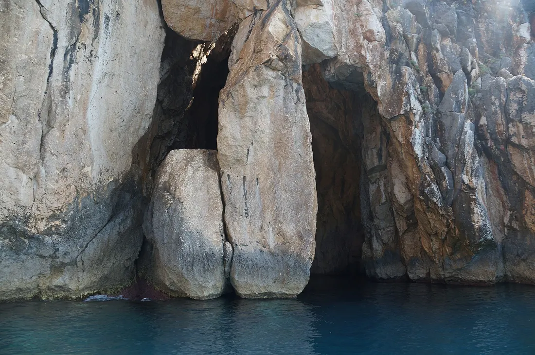 Pale limestone cliff with a sea cave at the water line near Dhërmi