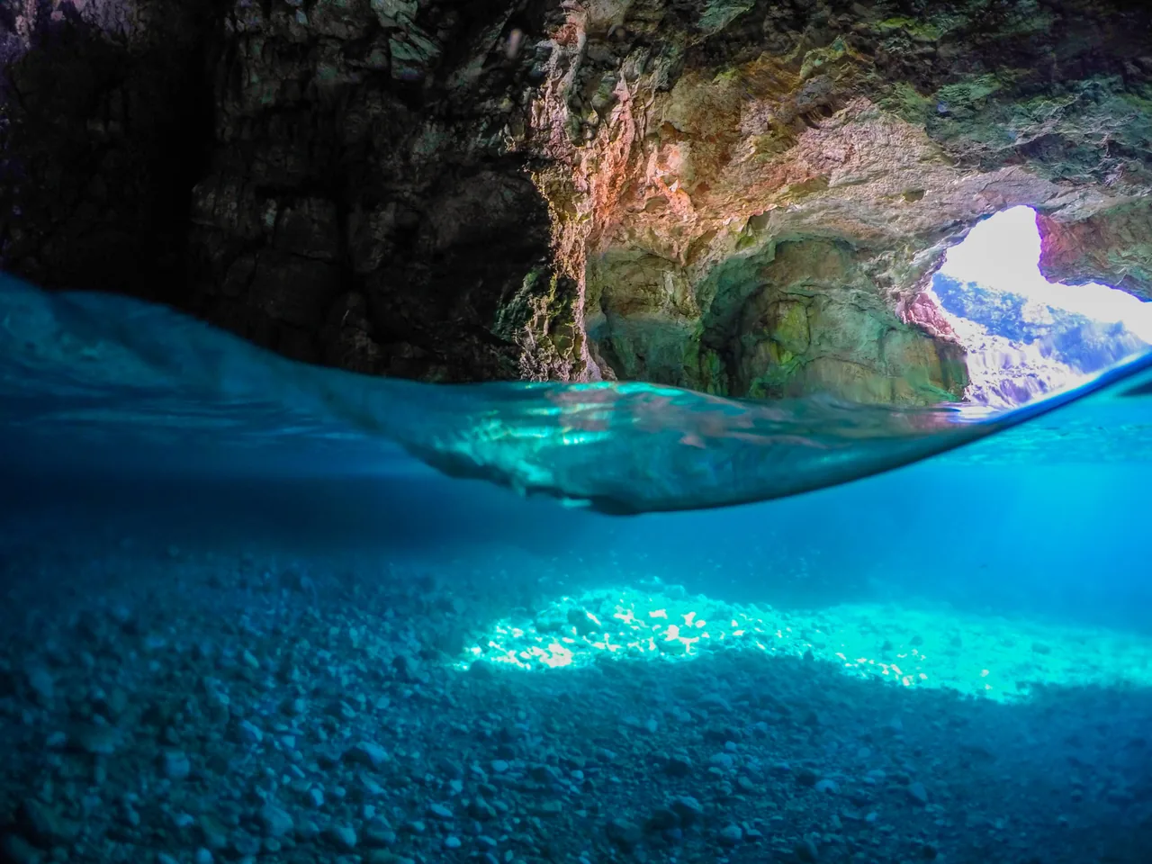 Split-level view inside a sea cave on the Karaburun peninsula with clear turquoise water and a bright opening to the sea