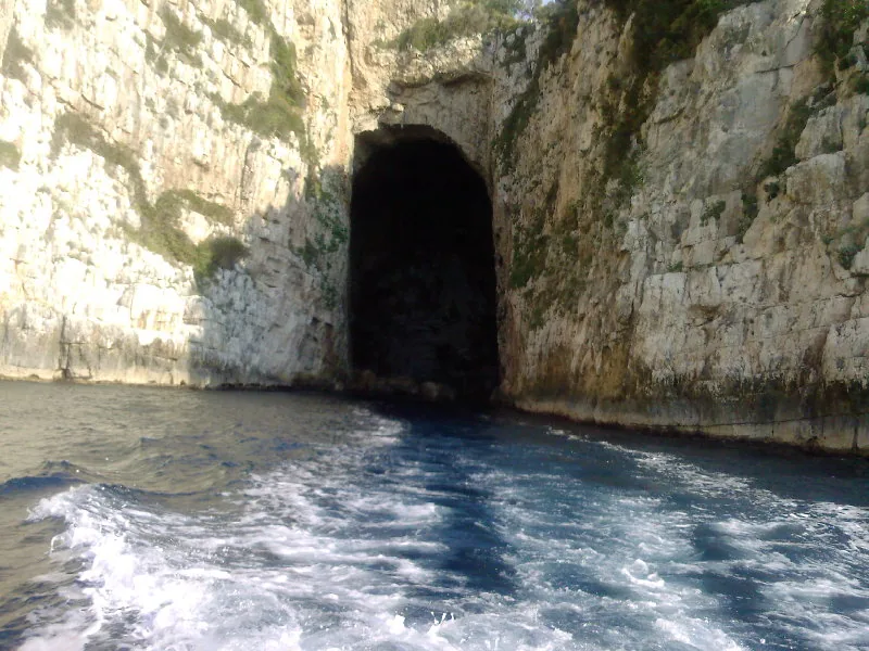 The dark arched entrance of Haxhi Ali Cave in the limestone cliffs of Karaburun seen from a passing boat