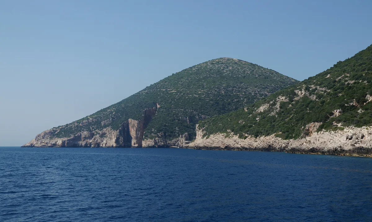Vertical limestone cliffs and dark blue water along the western coast of Sazan island