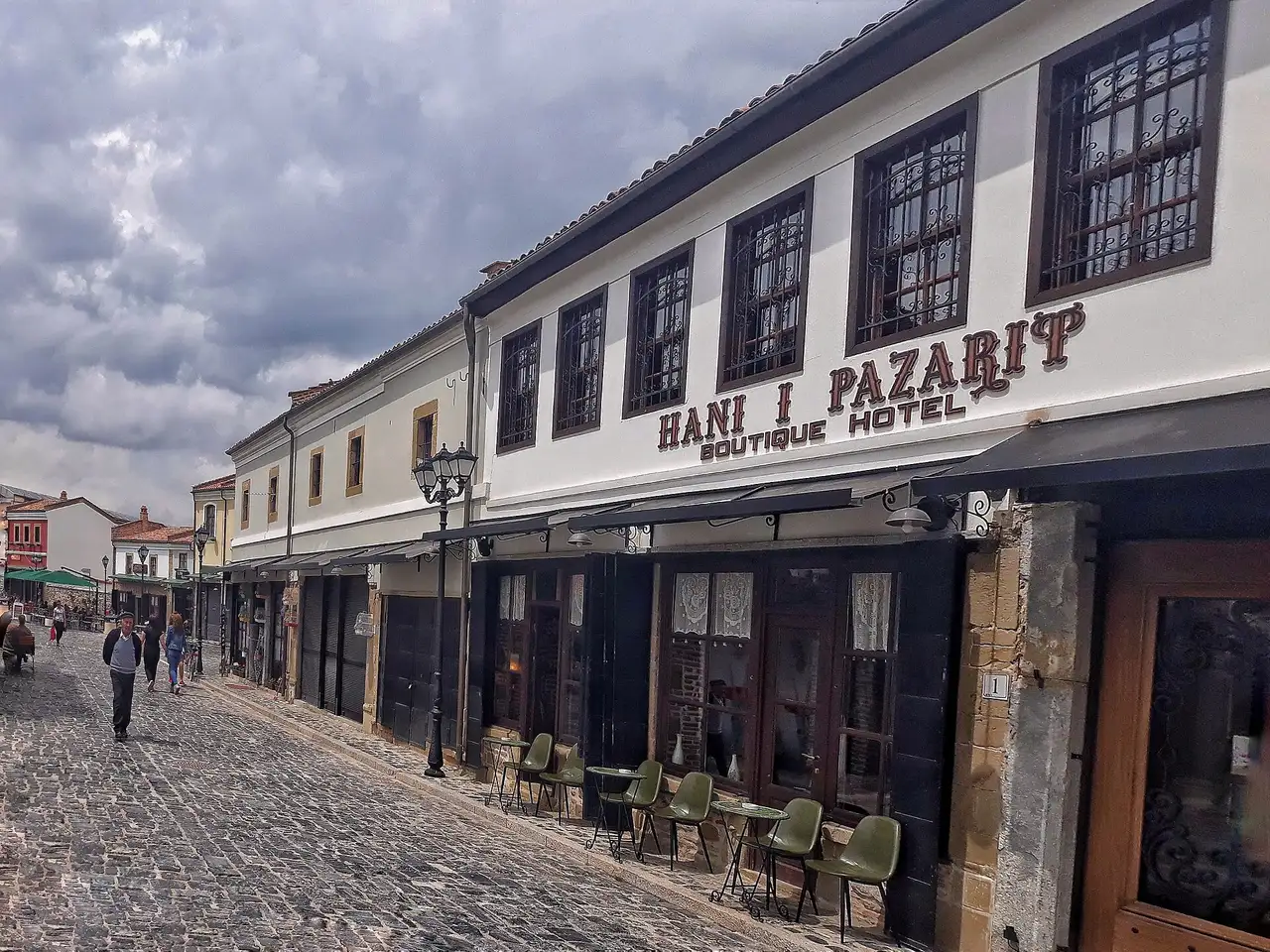 A tree-lined street of low buildings in central Korça on a bright day