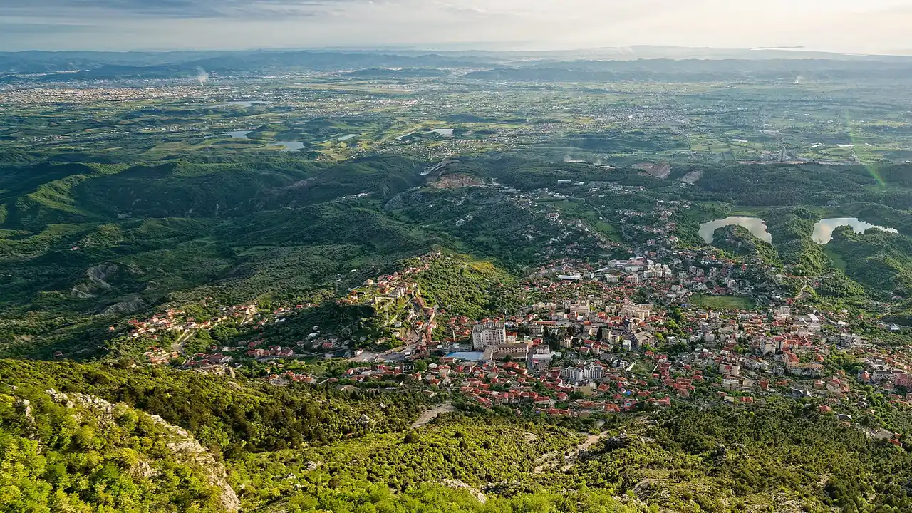 Kruja town spread across the mountainside above the coastal plain, seen from high on Mount Krujë with the castle rock on the left