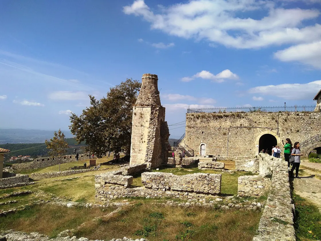 The ruined stone tower of the old Turkish bath inside Kruja Castle, with archaeological wall foundations and the fortress gate beyond