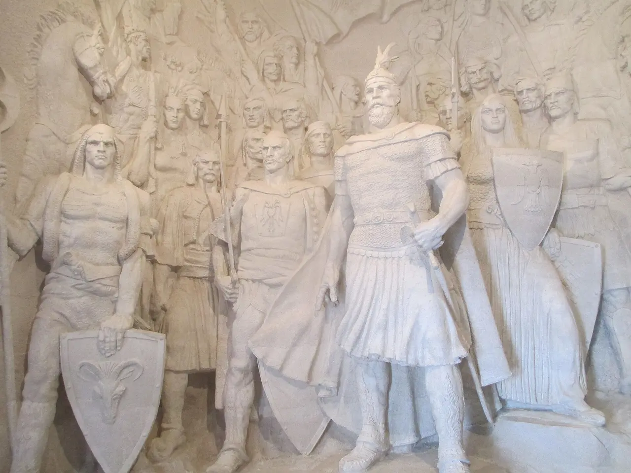 A large white sculpted relief inside the Skanderbeg Museum showing Skanderbeg in armour and helmet surrounded by his warriors with spears and shields