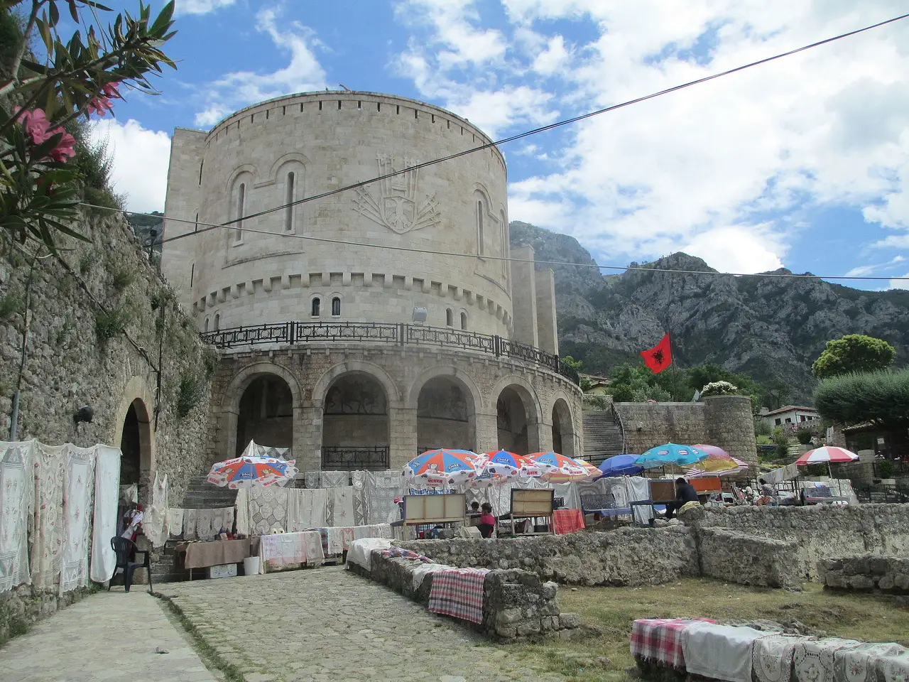 The round pale-stone tower of the Skanderbeg Museum inside Kruja Castle, with the Skanderbeg coat of arms carved on the facade and market stalls in front
