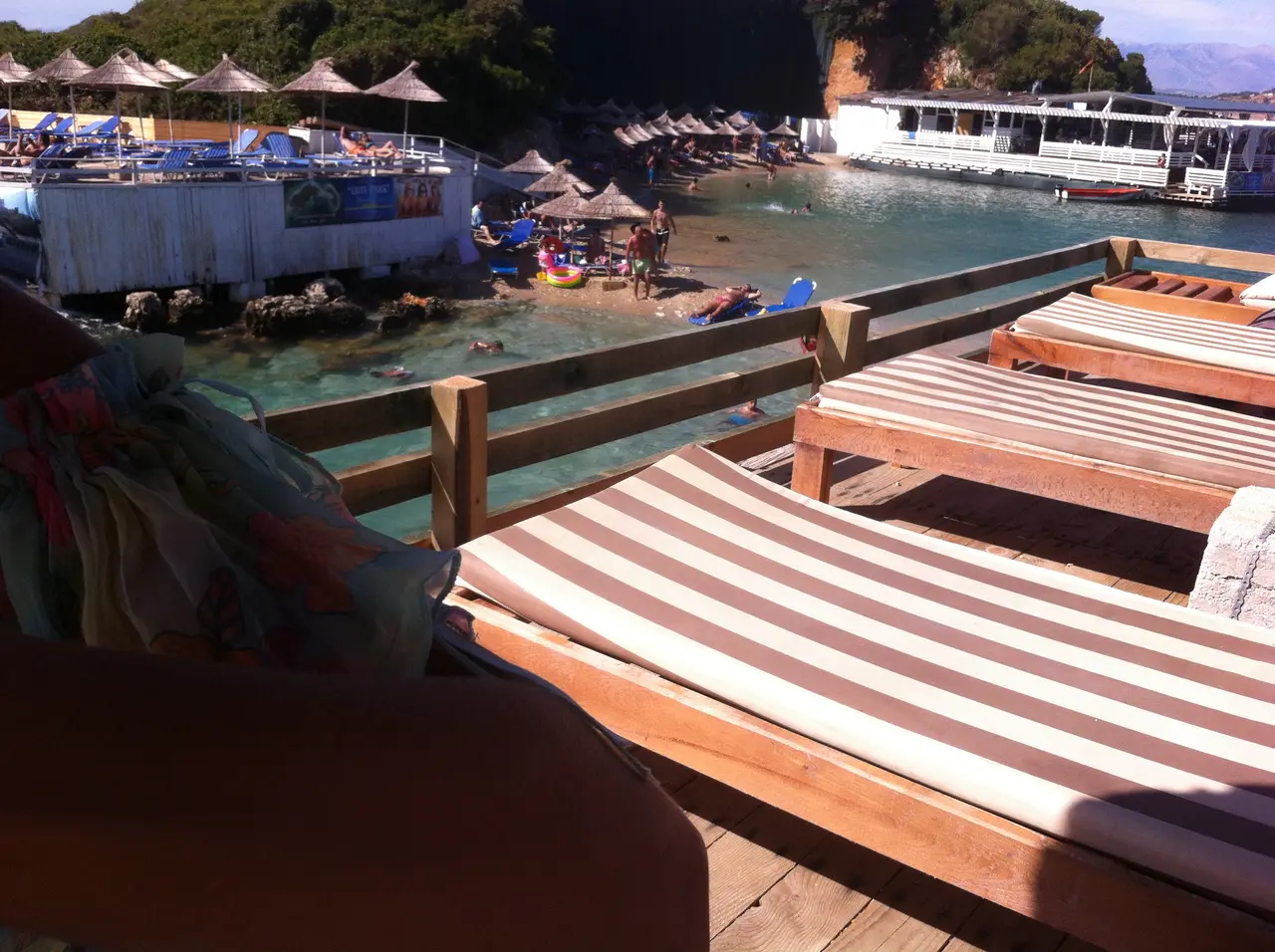 Sun-loungers and straw parasols on a Ksamil beach beside a small turquoise bay and boats