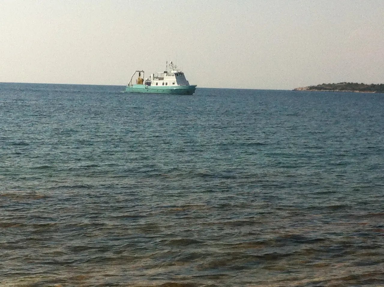 A small boat on the calm turquoise water off a Ksamil beach with an islet in the distance