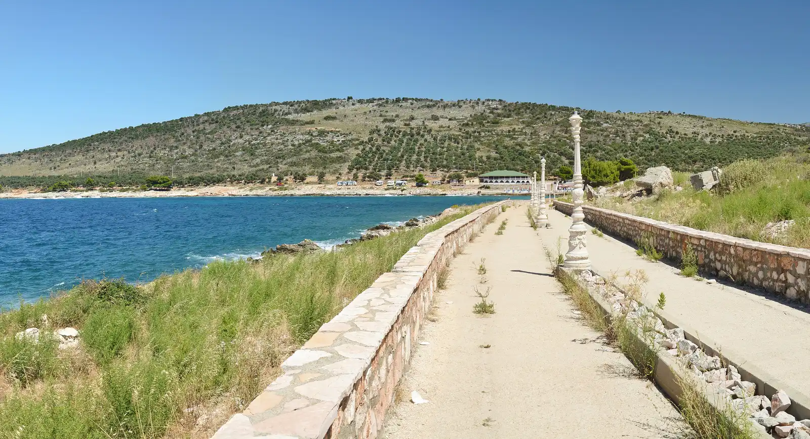 A stone seafront promenade at Ksamil running along the coast past a small beach