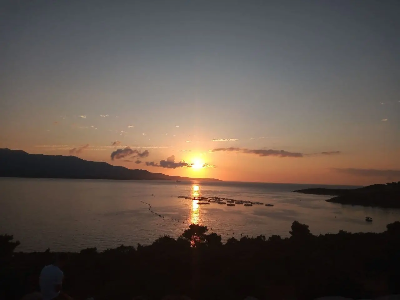 Sunset over the bay and islets at Ksamil with fish farms on the calm water