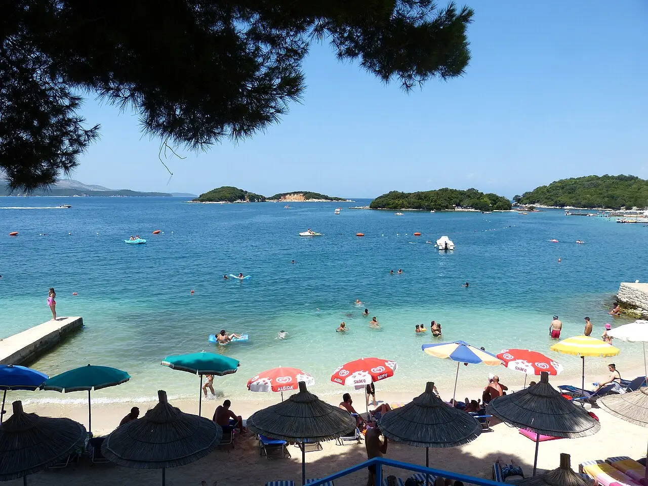 A sandy Ksamil beach with clear shallow water and an islet just offshore