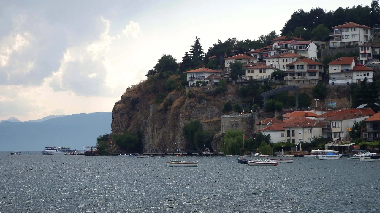 The old town of Ohrid stacked on its cliff above the lake, with rowing boats moored in the shallows below