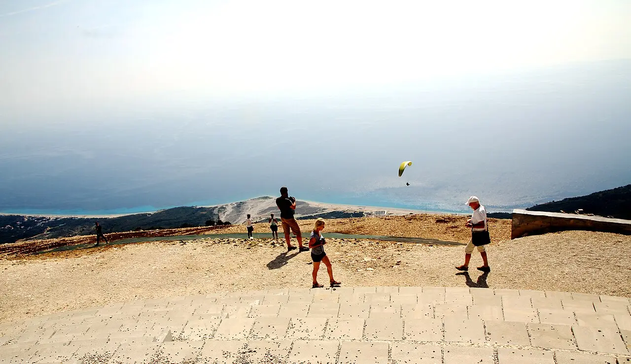 People at the Llogara viewing platform with a yellow paraglider in the air above the coast far below