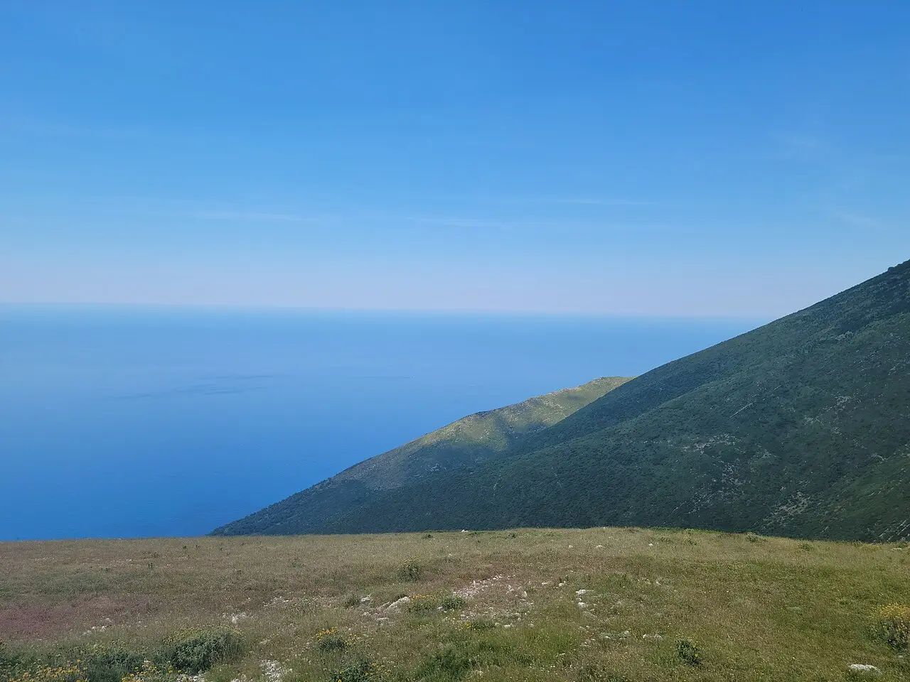 A deep blue expanse of the Ionian Sea seen from a green mountain slope high on the Llogara Pass