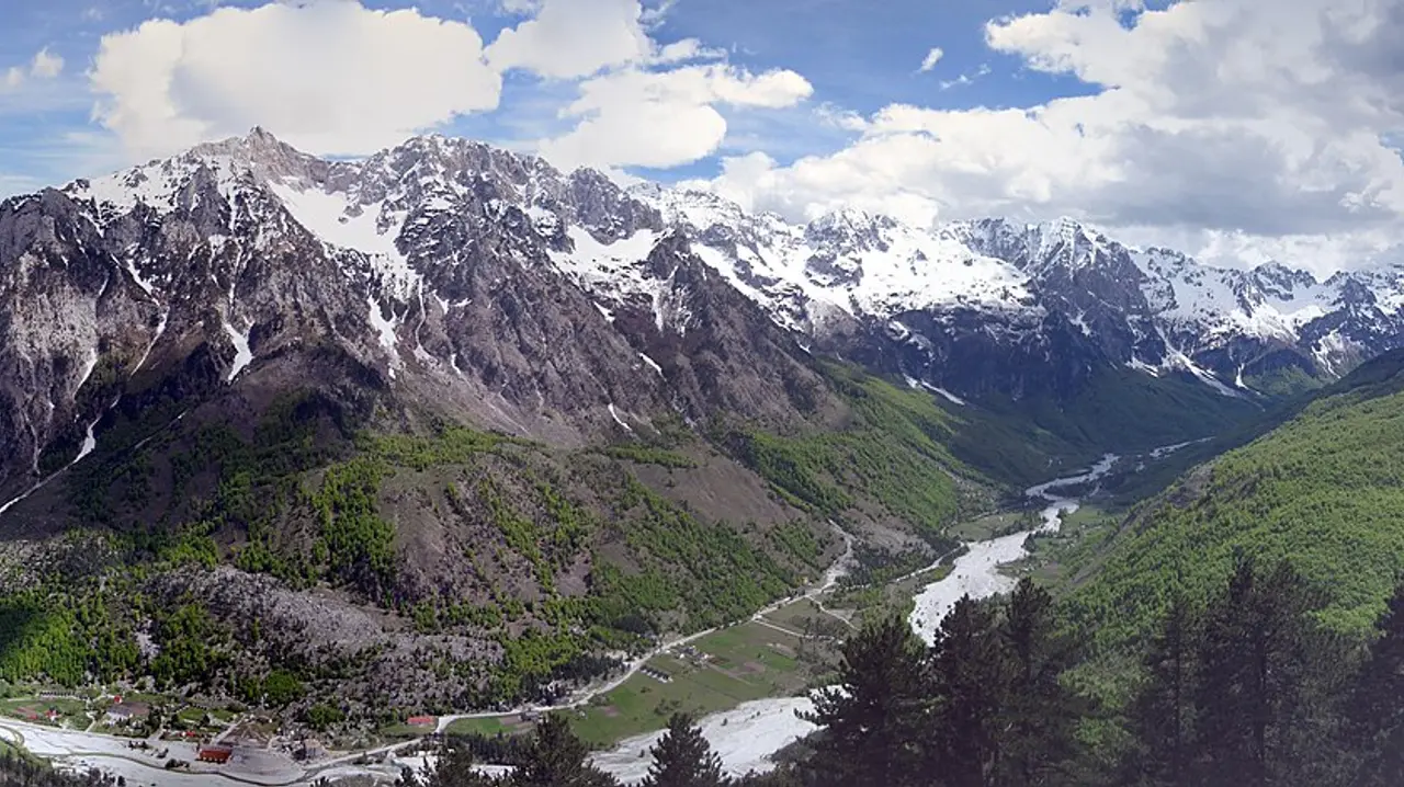 The Valbona valley in the Albanian Alps with snow-capped peaks above green forest and a braided river