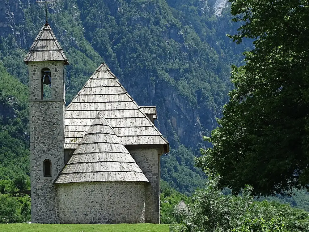 The stone church of Theth village with its wood-shingle roof below the cliffs of the Accursed Mountains