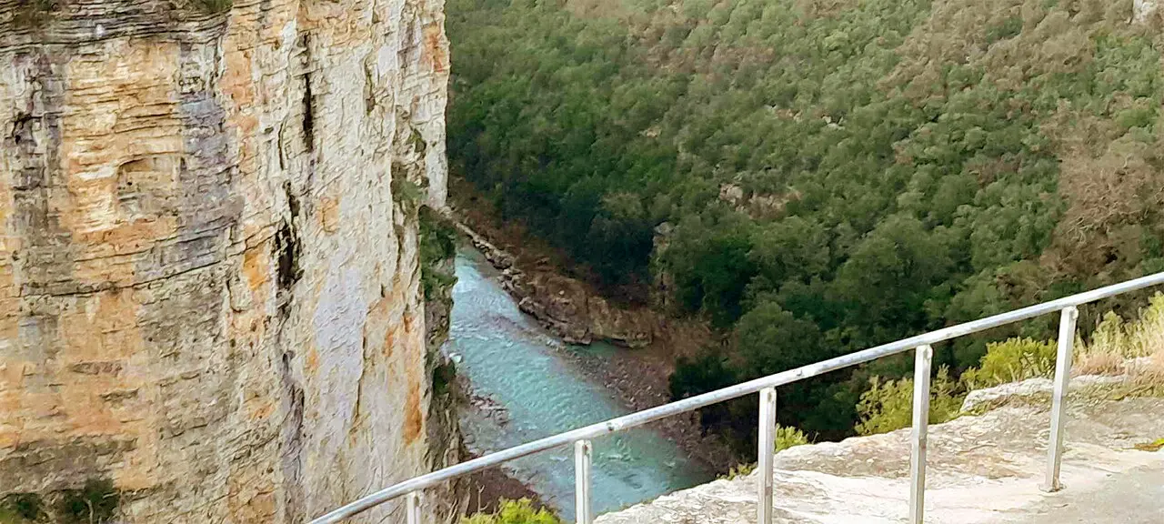View from a railed bridge down a sheer canyon wall to the turquoise Osum river below