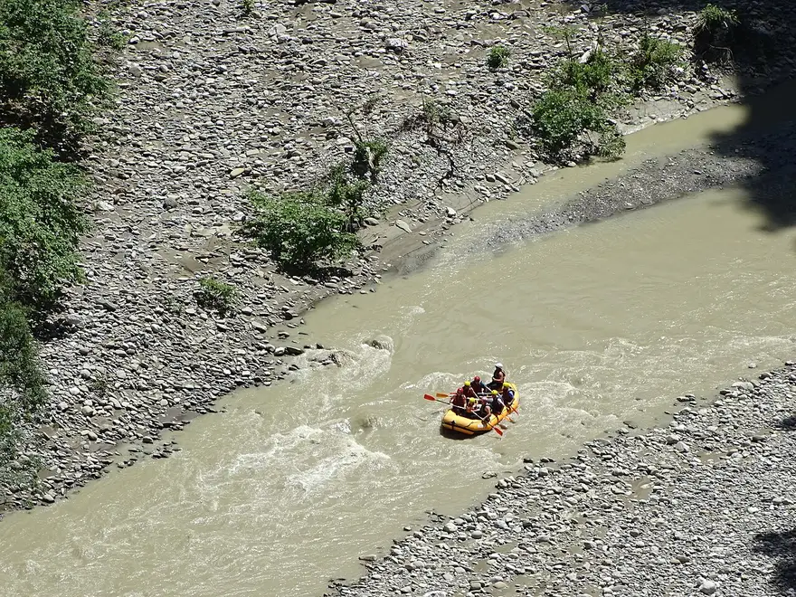 A yellow raft with paddlers running a shallow rapid on the Osum river between gravel banks