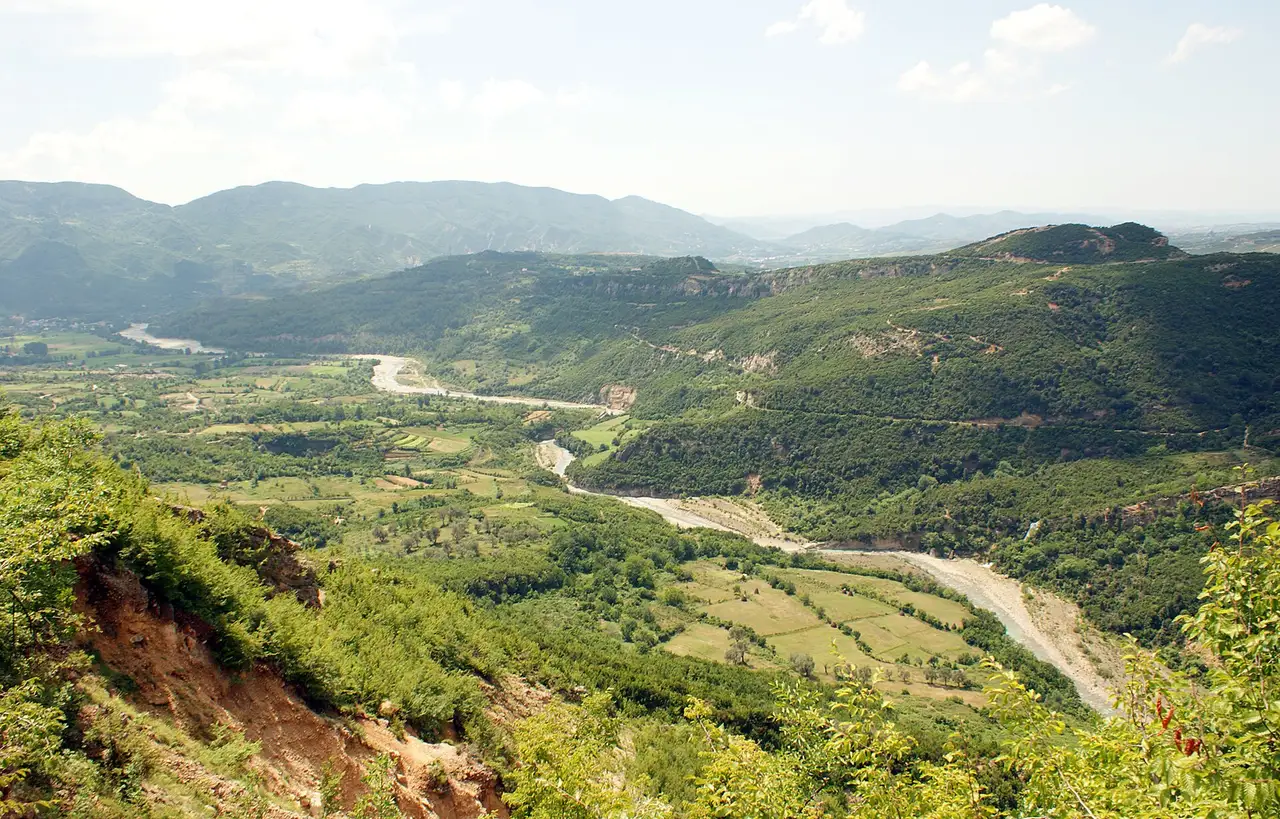 The Erzen river winding between pale gravel banks through a green valley, with wooded ridges on both sides