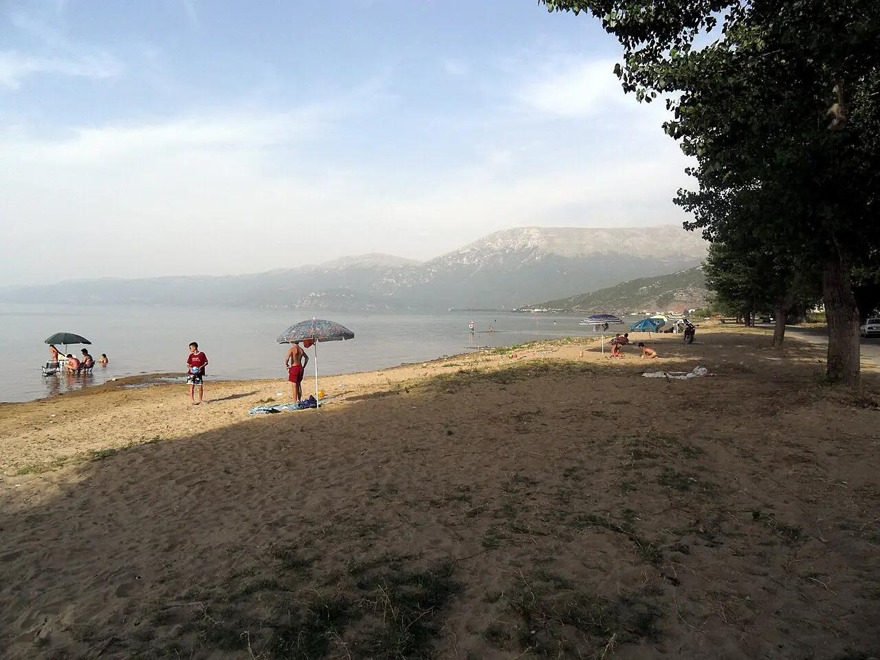 A pebble and sand beach at Pogradec on Lake Ohrid with swimmers, an umbrella and mountains across the water