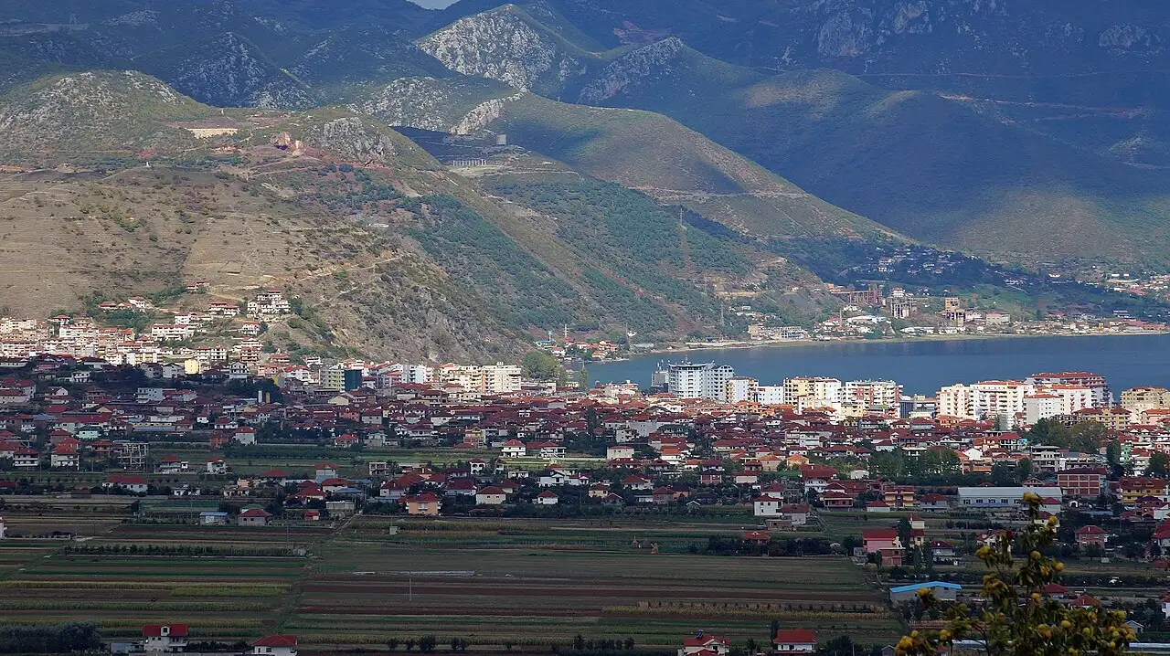The town of Pogradec spread along the shore of Lake Ohrid with mountains behind and green fields in the foreground