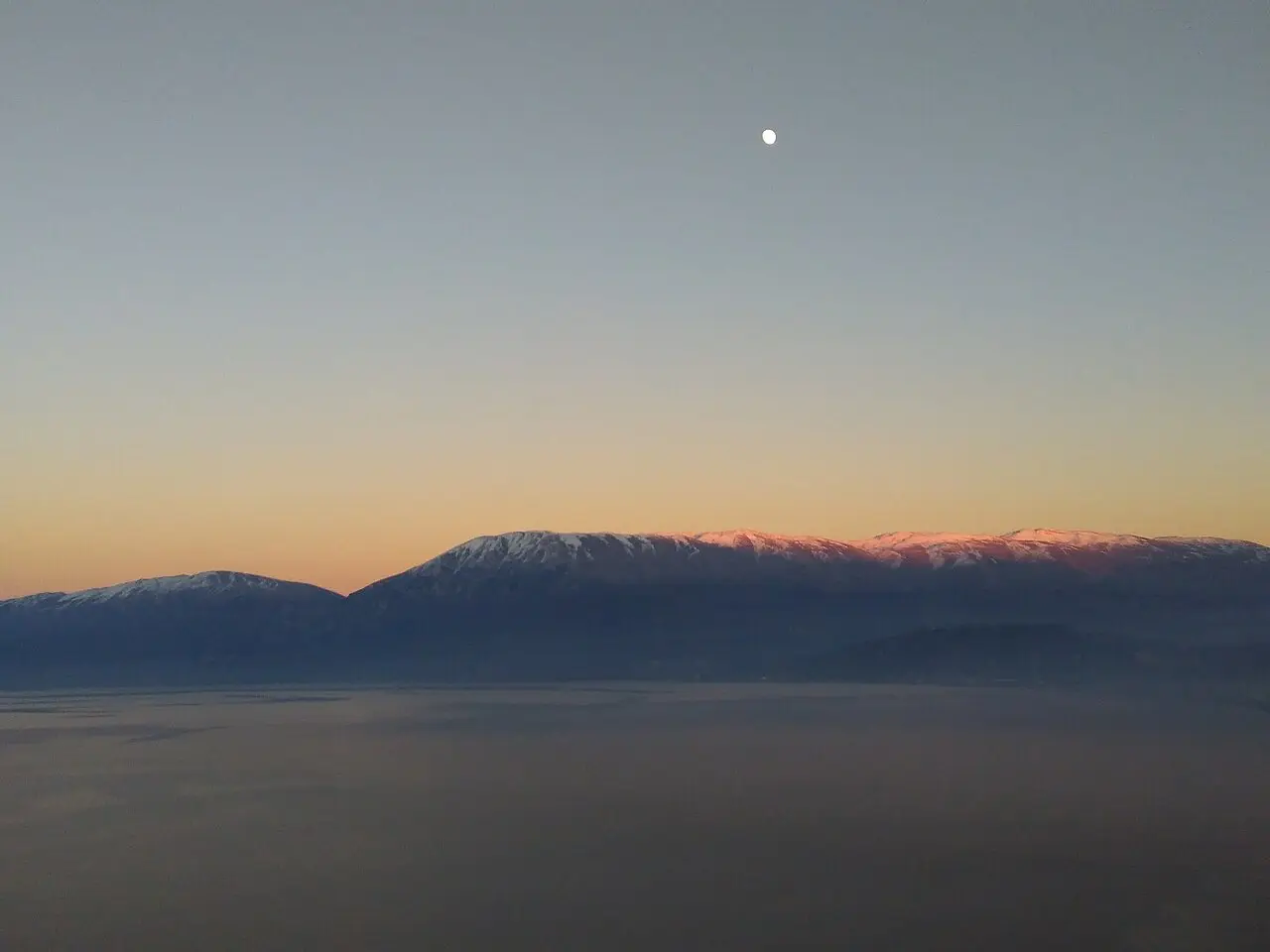 Dusk over Lake Ohrid from Pogradec with snow-capped mountains across the water and the moon rising