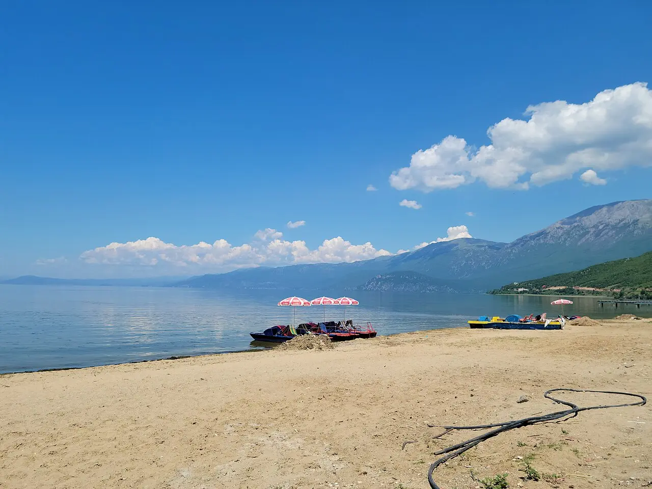 Pedal boats and umbrellas on a beach at Pogradec with the wide blue expanse of Lake Ohrid