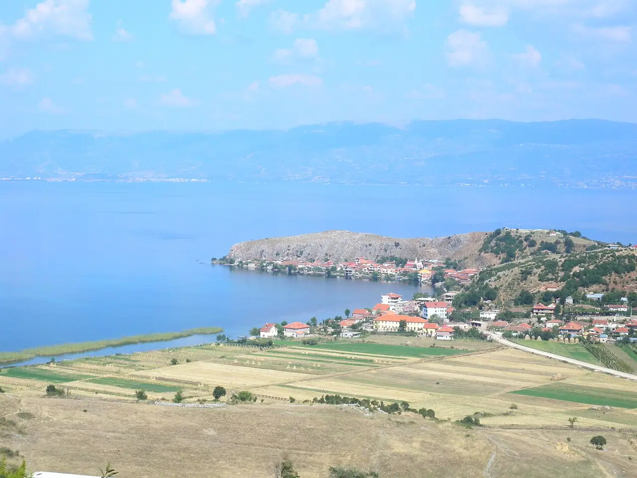 The village of Lin on its green peninsula reaching into the blue water of Lake Ohrid, with fields in front