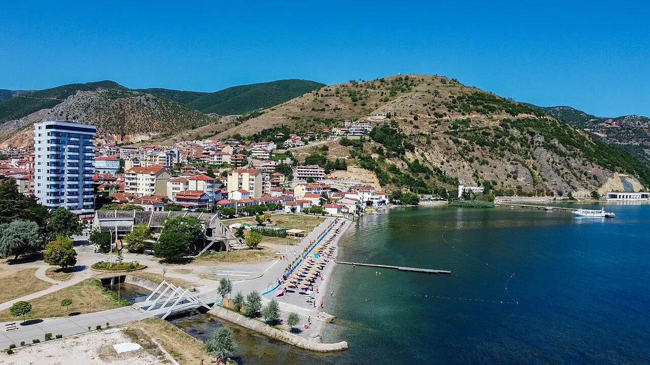 Aerial view of Pogradec town, its beach and pier on Lake Ohrid with the hill behind