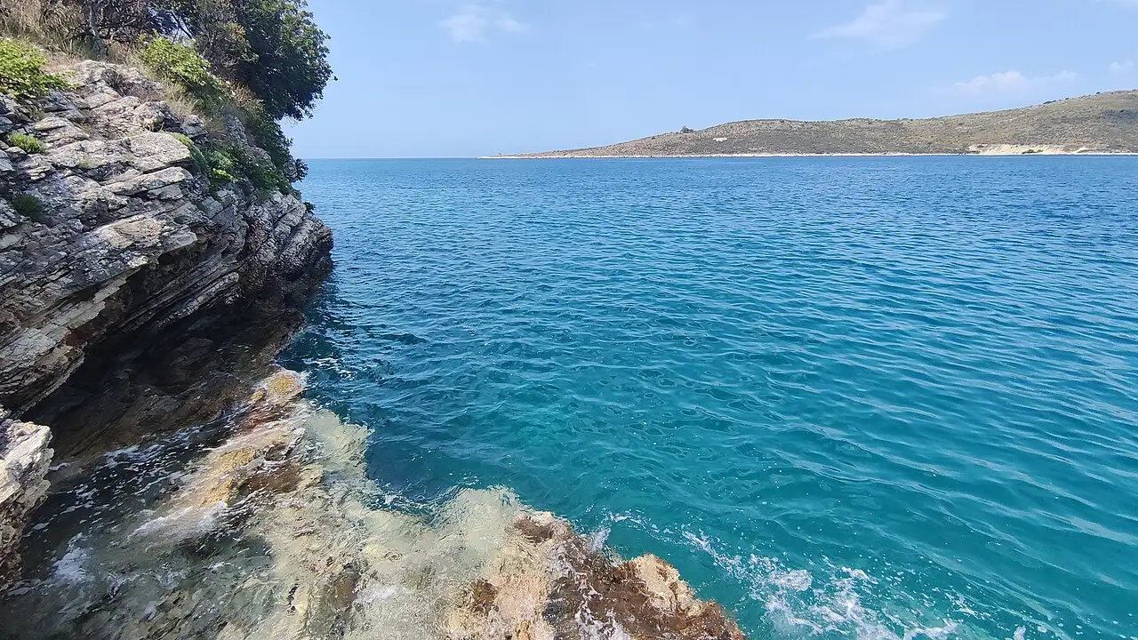 Clear turquoise water breaking over layered limestone rocks at the edge of Porto Palermo bay