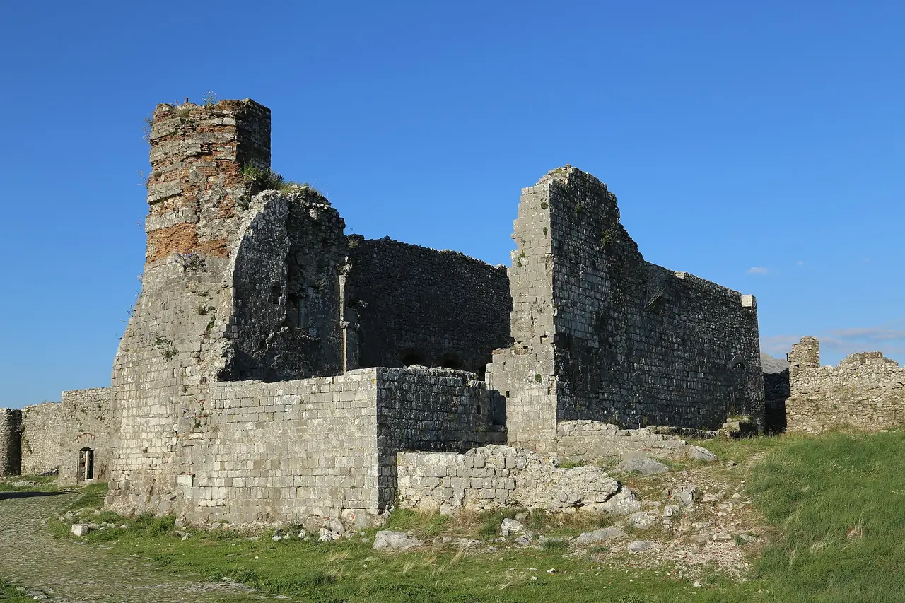 Roofless stone ruins inside Rozafa Castle, a square tower with a band of reddish brick under a clear sky