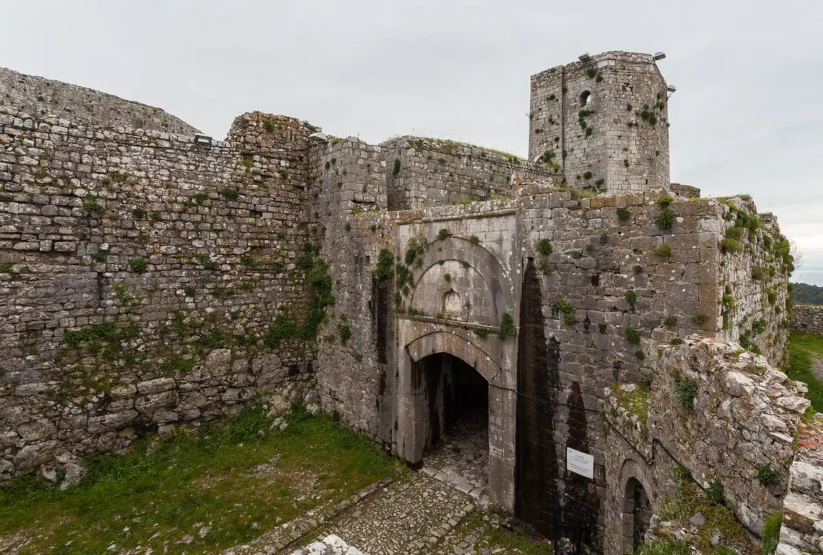 The pointed-arch main gate of Rozafa Castle in a thick limestone wall, with a polygonal tower behind