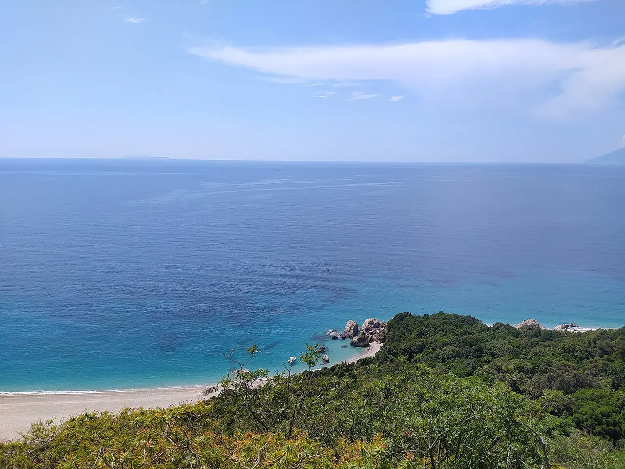 White pebbles and clear blue water at Krorez Beach backed by green hills